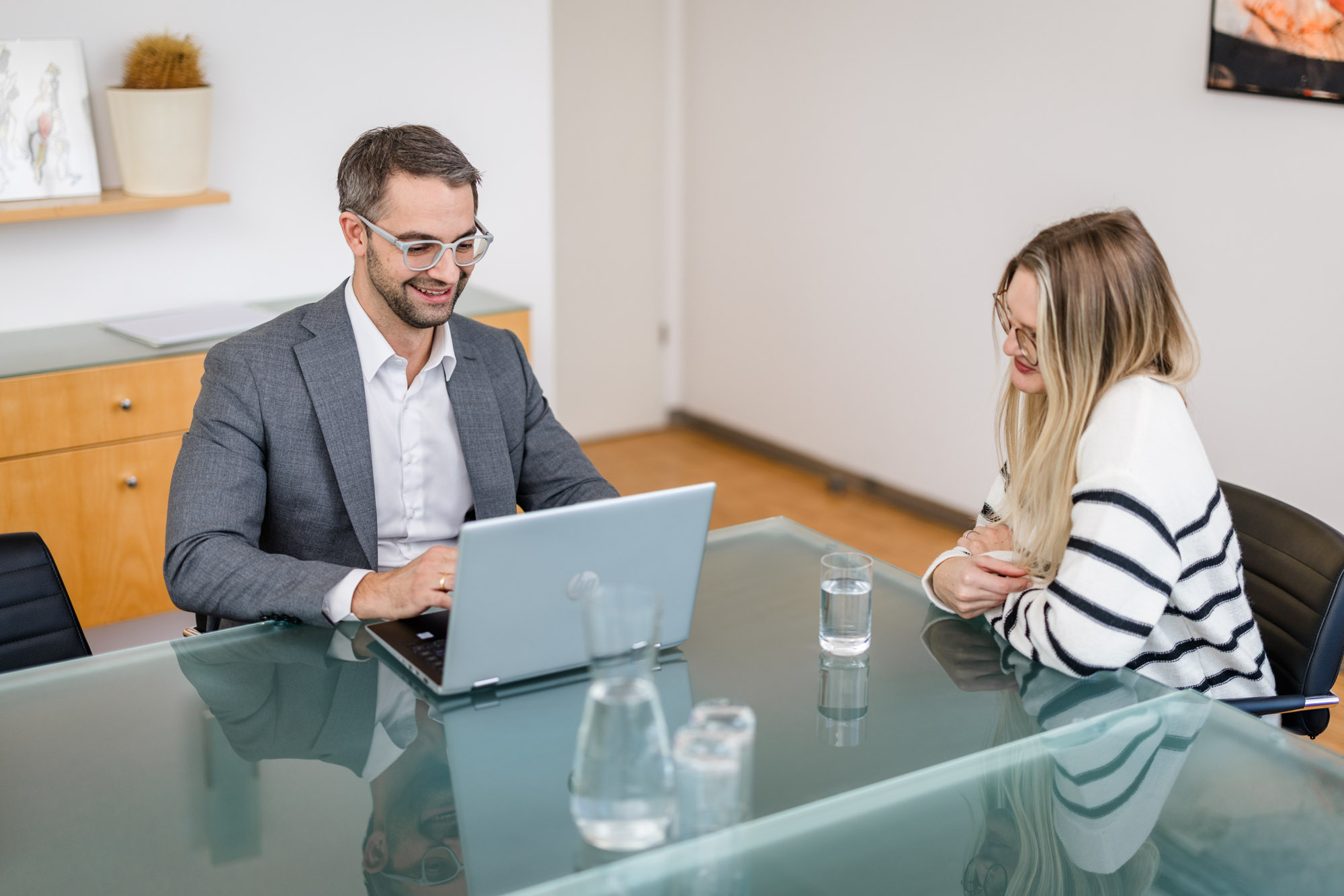 Anwalt und Dame sitzen am Tisch und besprechen etwas mit einem Laptop
