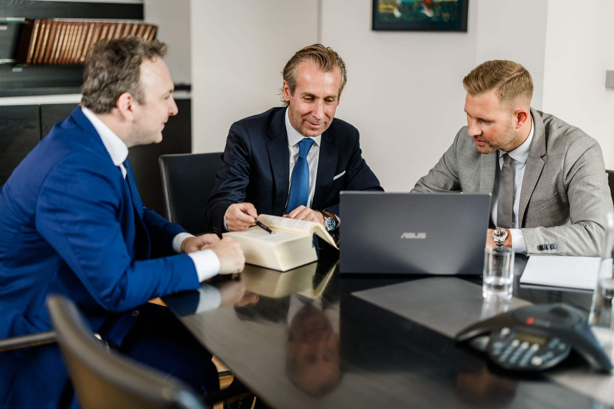 Drei Männer sitzen an einem Tisch mit Laptop und Gesetzesbüchern
