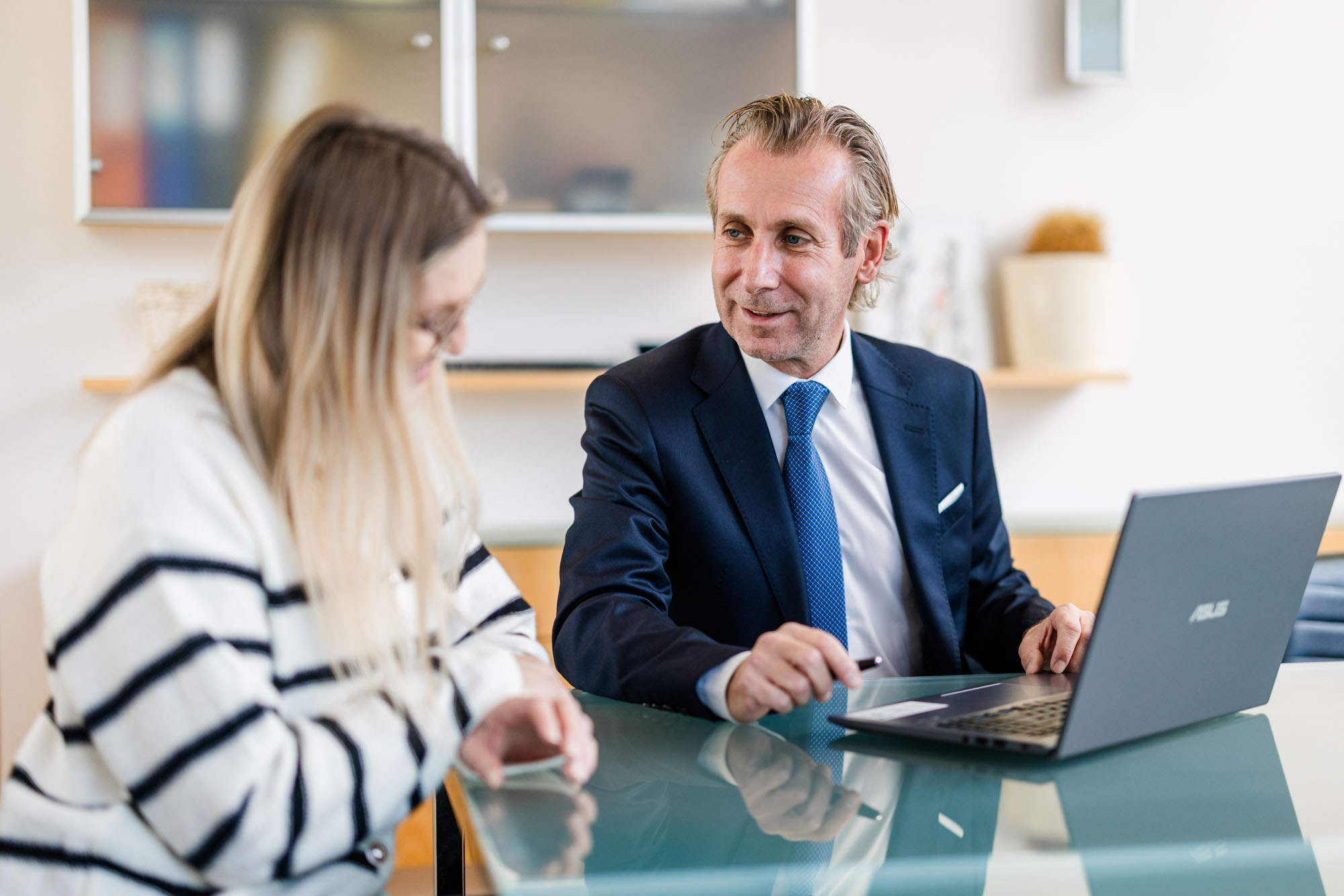 Anwalt und Dame sitzen an einem Tisch mit Laptop und sprechen miteinander