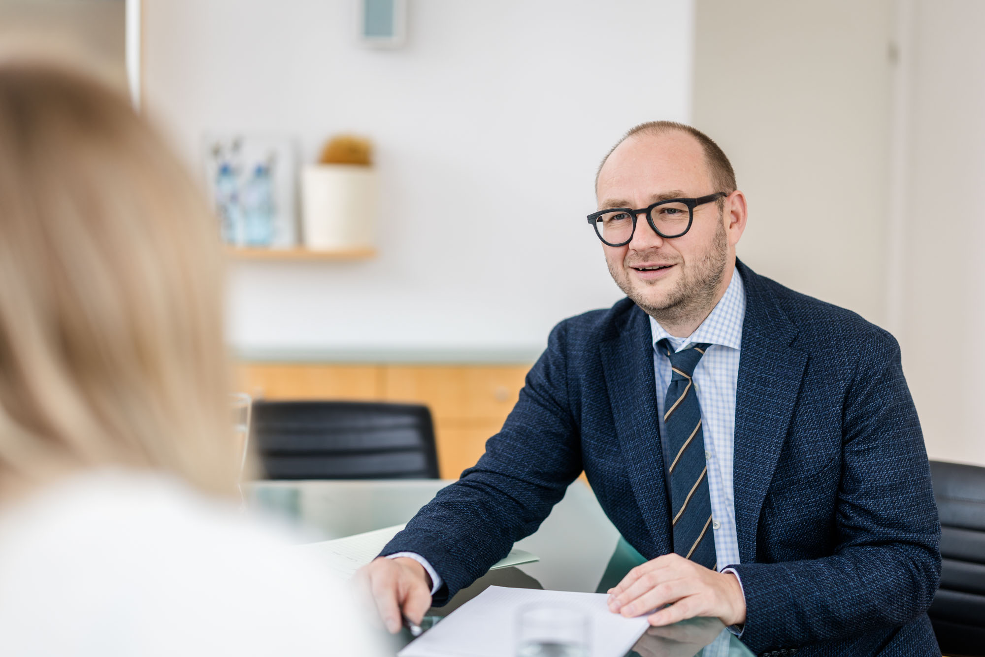 Anwalt sitzt an einem Tisch mit einer Frau und blickt in die Kamera