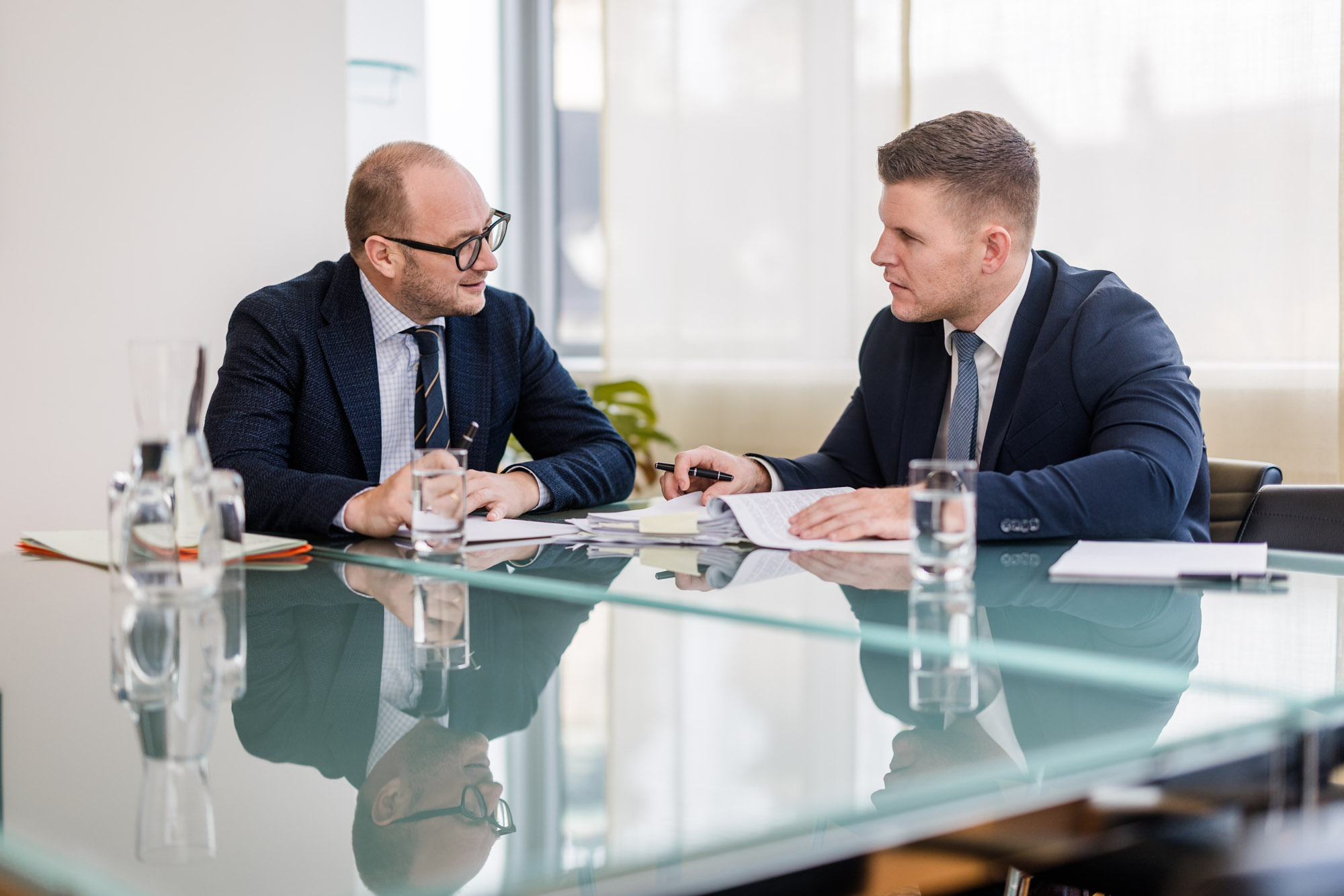 Zwei Männer sitzen an einem Glastisch und führen ein Gespräch