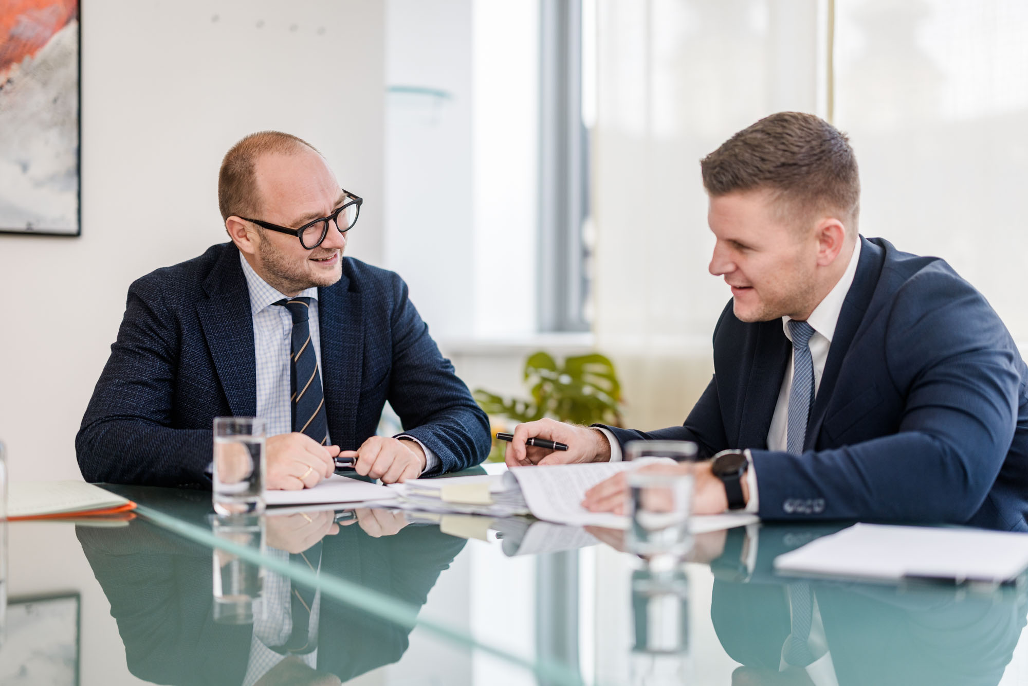 Zwei Anwälte sitzen an einem Tisch und sprechen miteinander über Dokumente, die am Tisch liegen
