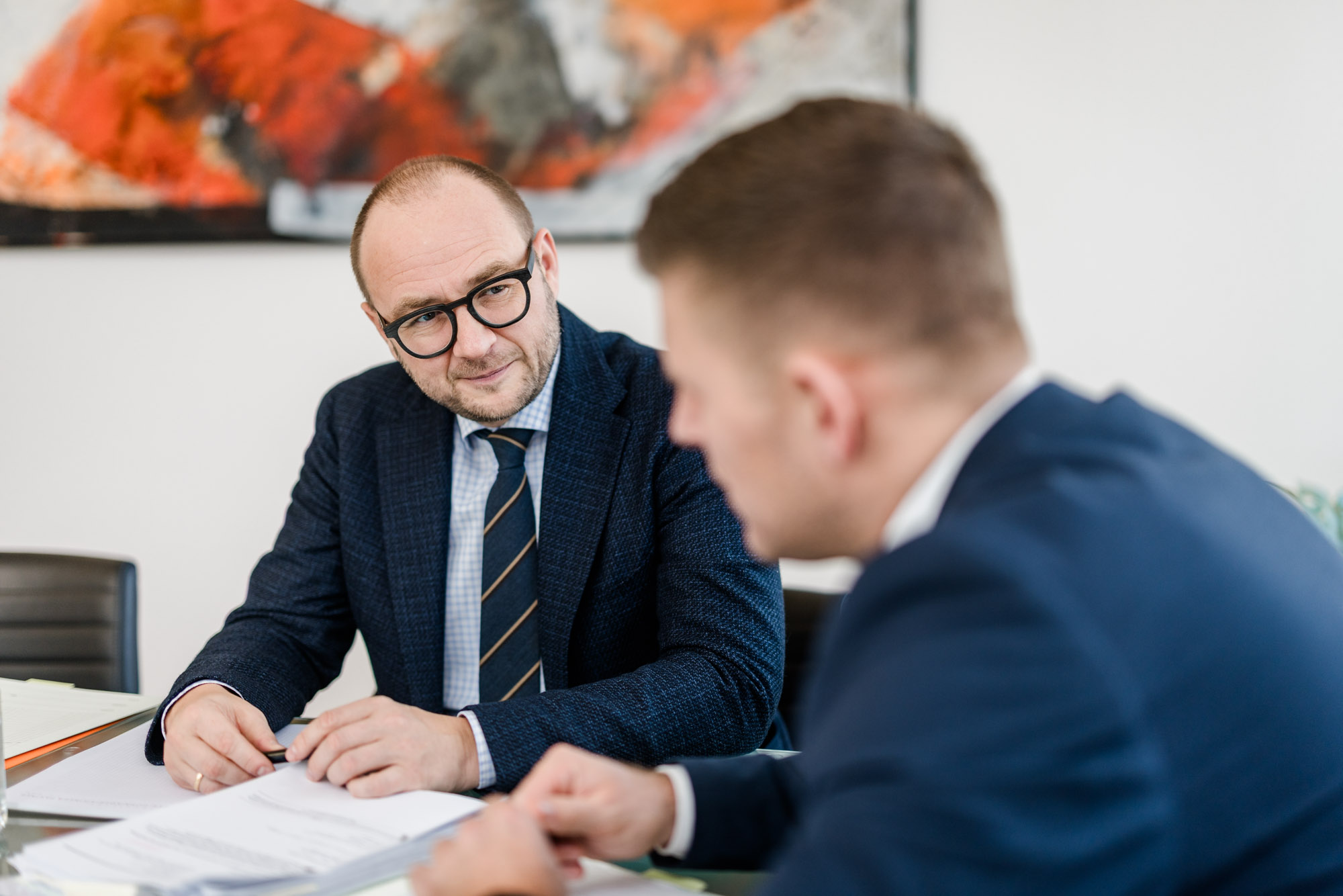 Anwalt sitzt am Tisch mit Unterlagen und schaut anderen Anwalt an.
