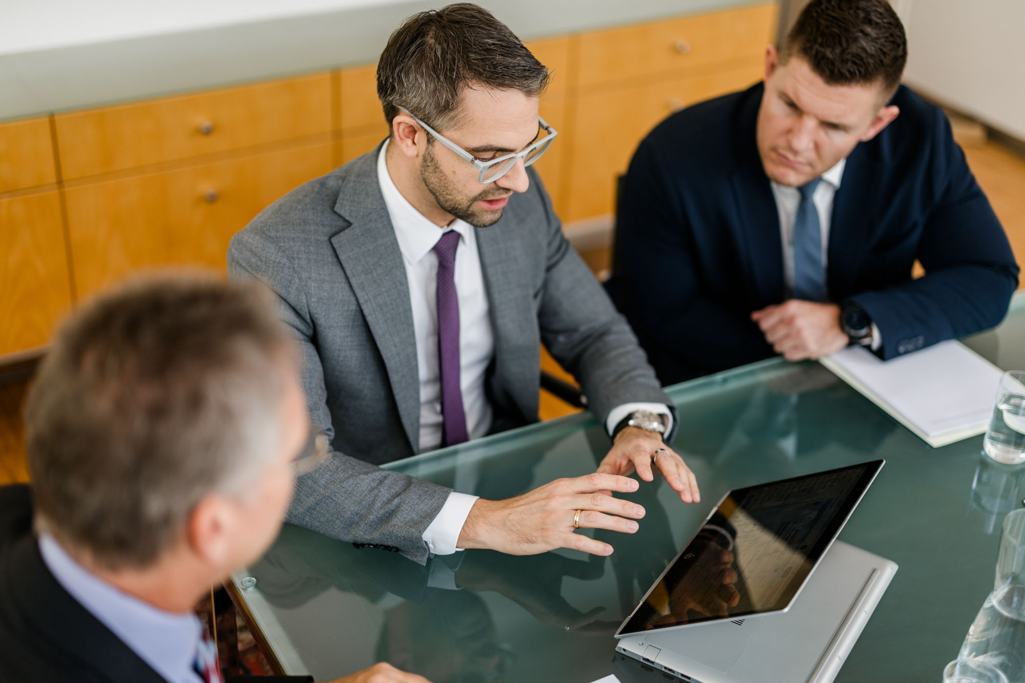 Anwalt deutet auf ein Tablet auf dem Tisch und erklärt zwei weiteren Personen etwas